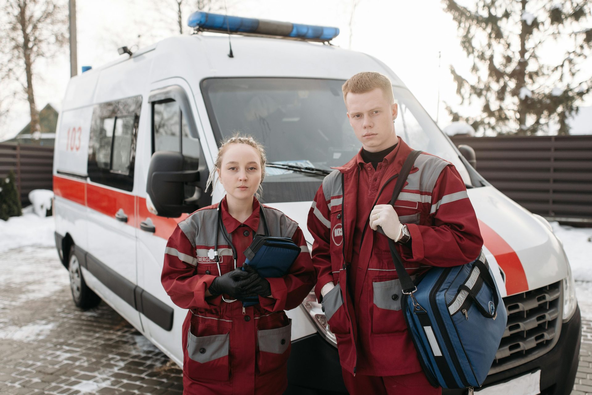 Two paramedics in uniforms standing by an ambulance in a winter setting, ready for emergency response.