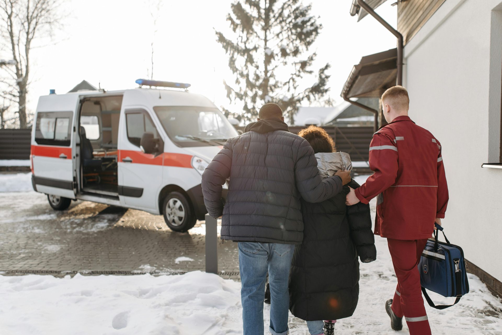 Rettungssanitäter geleiten im Winter eine Familie zu einem Rettungswagen und veranschaulichen dabei die notfallmedizinische Versorgung.