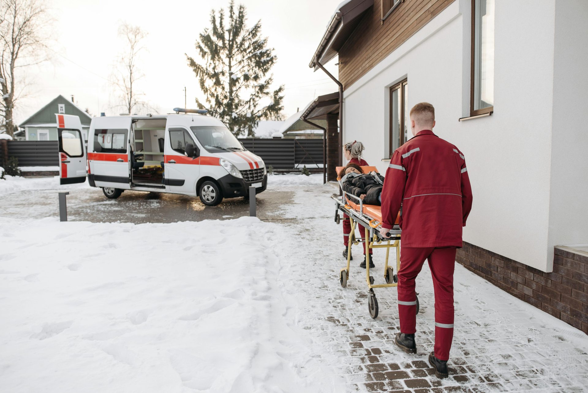 Paramedics transport a patient on a stretcher to an ambulance in a snowy residential area.